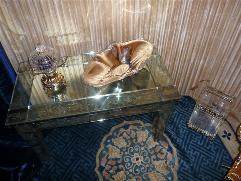 A terra, il nostro CESTINO serie RICCIOLO in finitura oro, con plexiglas inciso; Sul tavolino una realizzazione speciale dell'articolo VERSAILLES, scatola con coperchio: parti in metallo finitura oro, pietre blu.